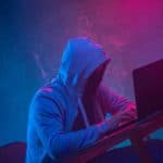 Hooded computer hacker stealing information with laptop
